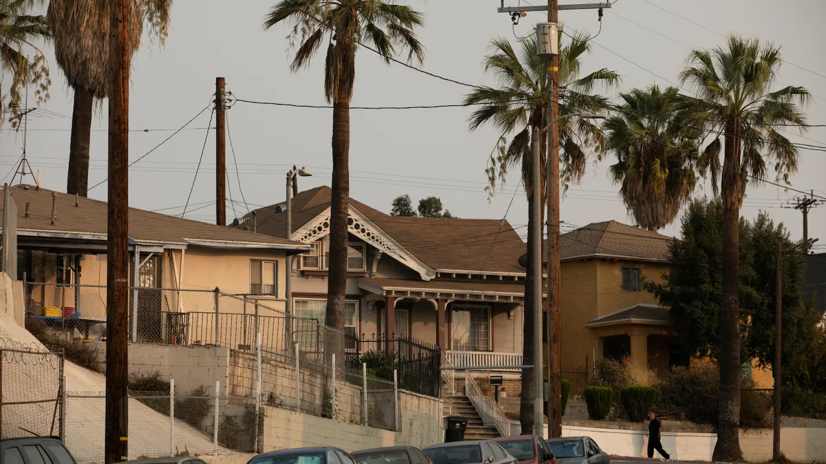 Closely spaced single-family homes with telephone poles, wires and palm trees lining the street.