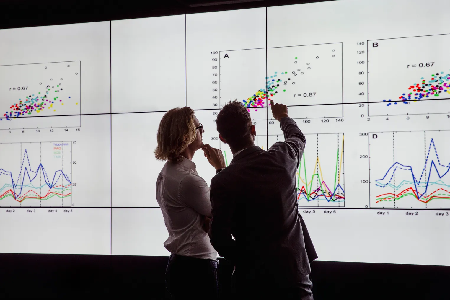 Business men in a dark room standing in front of a large data display