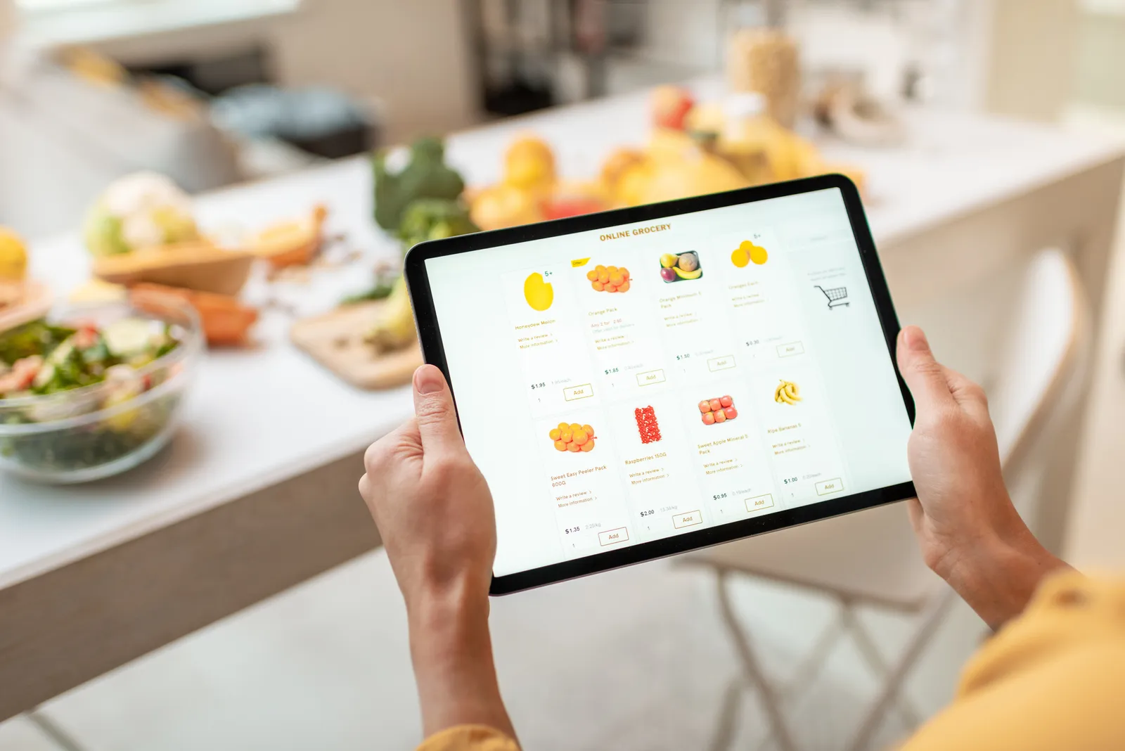 In a kitchen, close-up of hands holding a tablet with food on the screen.