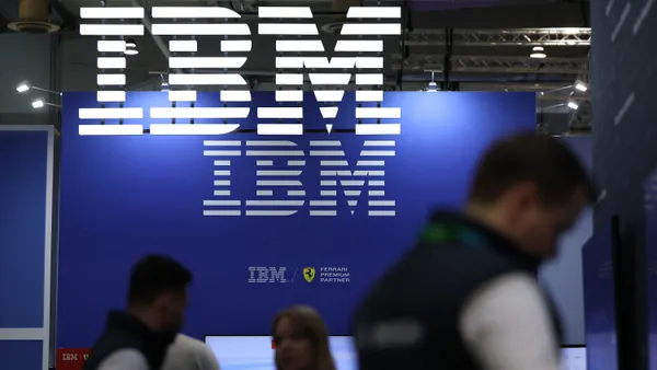 A blur of people walk by an illuminated sign featuring the IBM corporate logo.