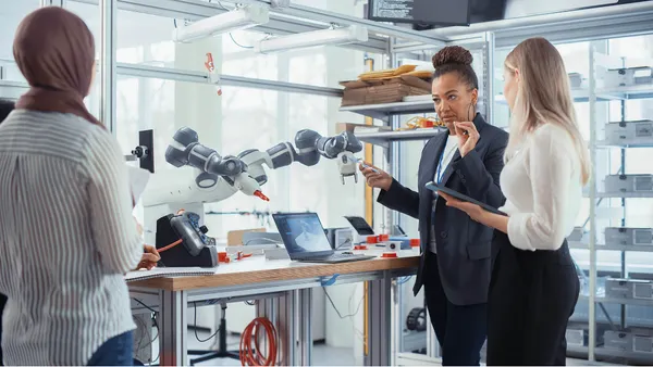 People Look at Robot Limb. Interns Hold Devices and Discussing.