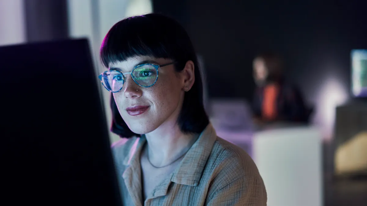 Business woman, computer seo work and coding of young employee with blue light and glasses. Digital code, female face and reading of a it employee at night planning with online ecommerce and ai data