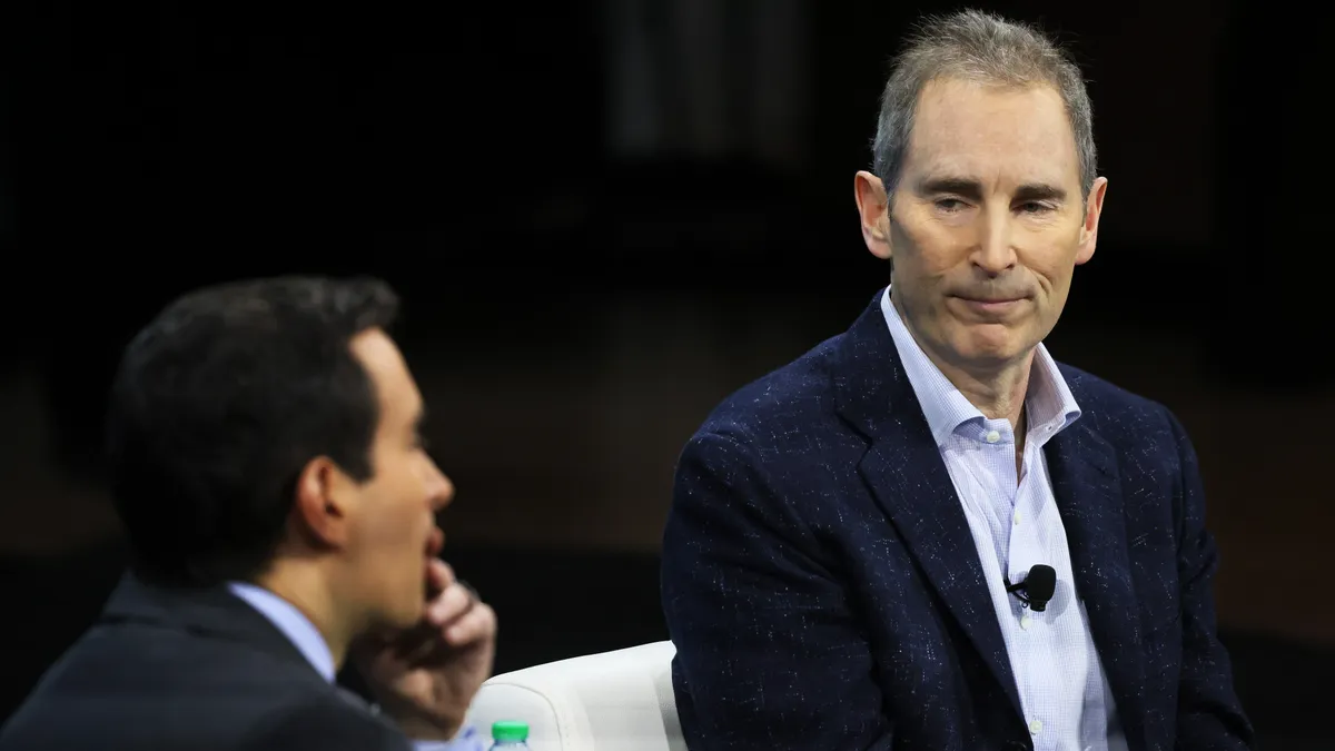 Andy Jassy (right) sits in a suit, looking at Andrew Ross Sorkin (left), also in a suit.