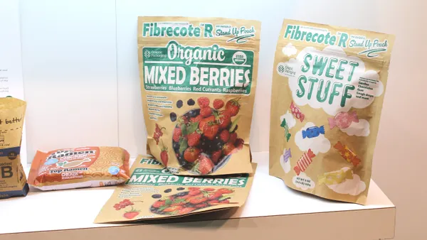 A variety of paper-based packaging with Graphic Packaging International's branding sits on a display shelf at a conference.