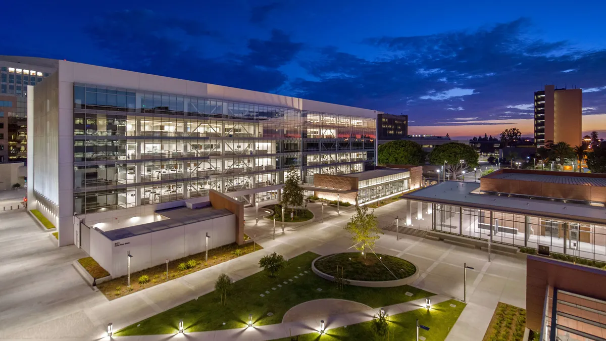 A rendering of a cluster of buildings with a green space in the middle at night. Walkways surround the area and the green space.