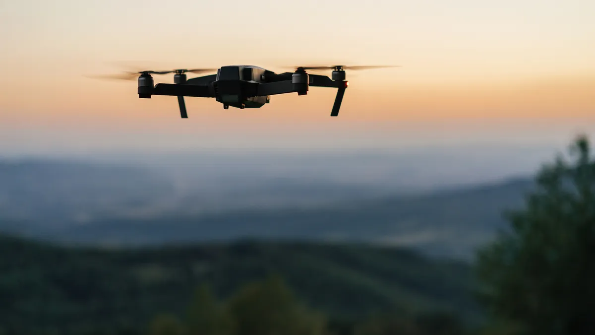 Drone hovers in front of blurred landscape at sunset