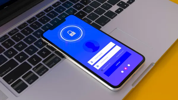 A smartphone with a cybersecurity application icon visible sits atop a PC keyboard.