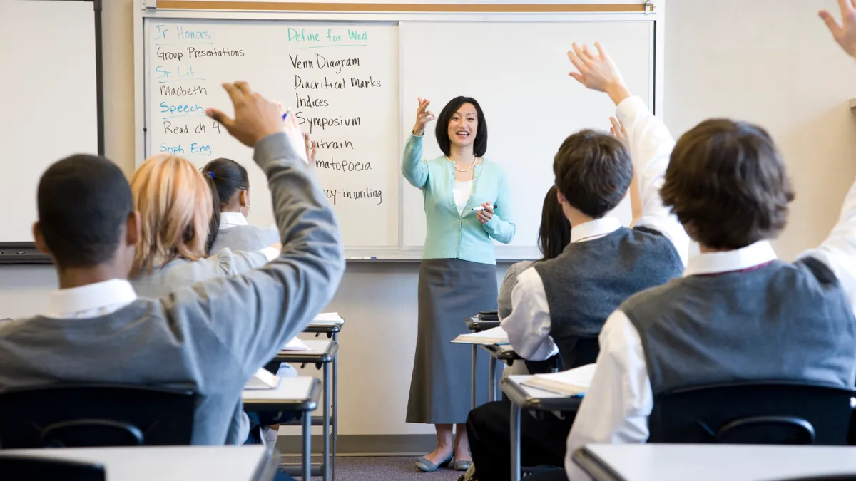 Students raise their hand in a school classroom as a teacher picks a student to speak