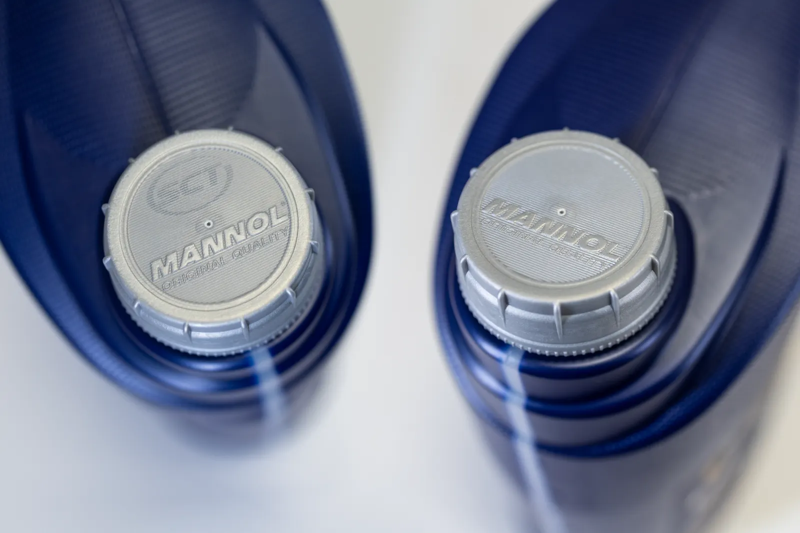 A closeup of two silver-colored caps on blue container that have Mannol branding embossed on the top.