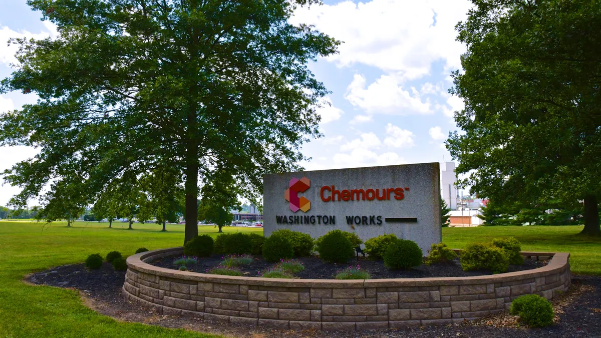 A gray sign with the orange, red and pink Chemours logo on it.