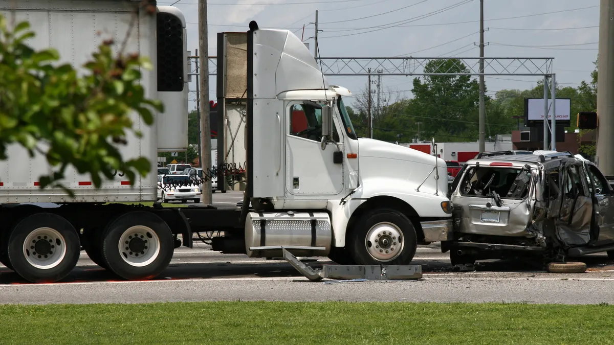 A white tractor-trailer is shown next a heavily damaged passenger vehicle.