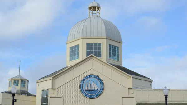 The front of a government building with an American flag on top under a blue sky with clouds.