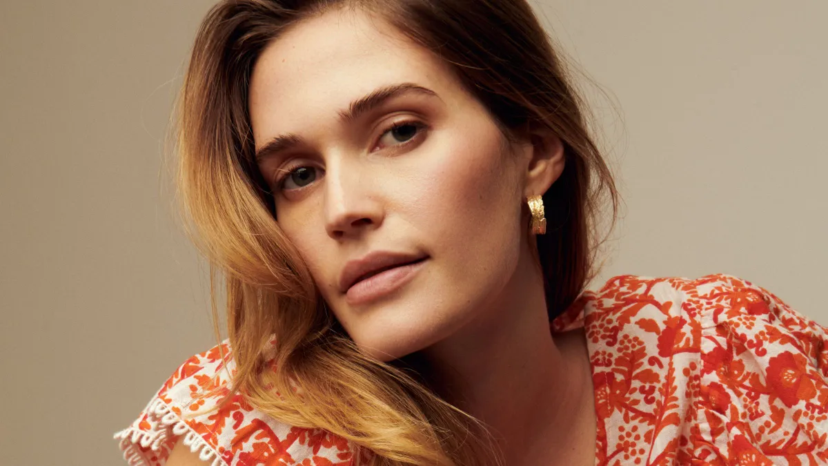 A person in a red and white floral top and goldtone hoop earrings faces the camera.