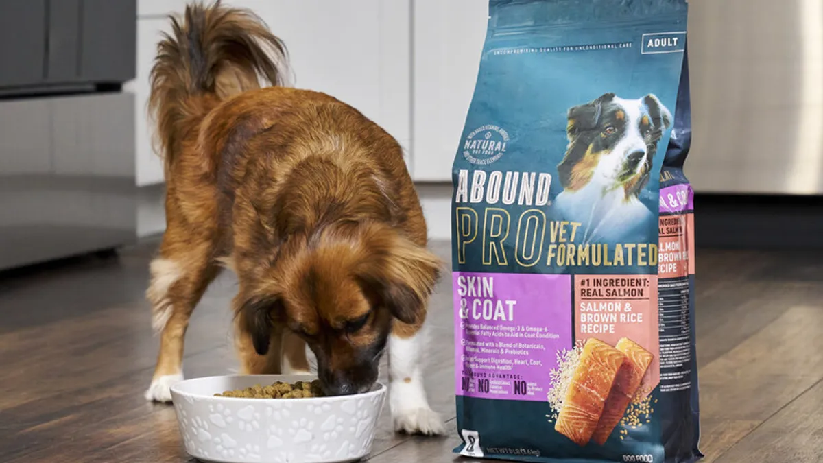 A dog eating dry food from a bowl next to the bag of dog food.