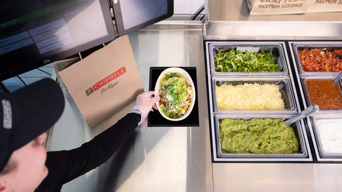 A worker lifts a filled bowl out of a test version of Hyphen and Chipotle's automated digital makeline.