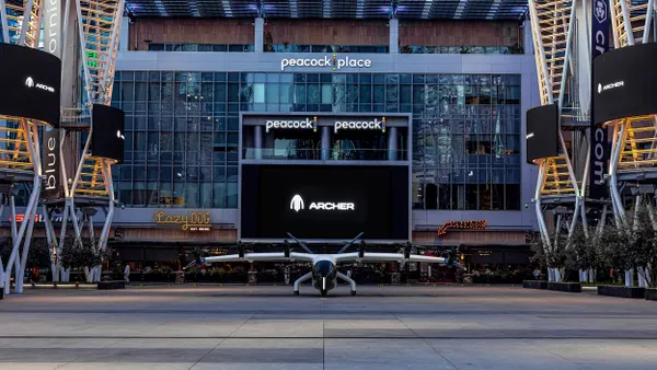 A small aircraft with six propellers on the ground in front of restaurants and entertainment venues.