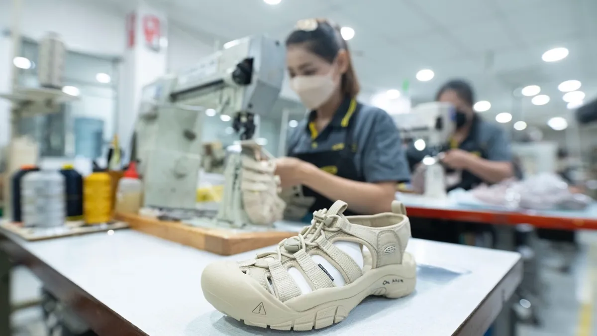 Behind a finished sandal sits a masked worker manning a sewing machine.