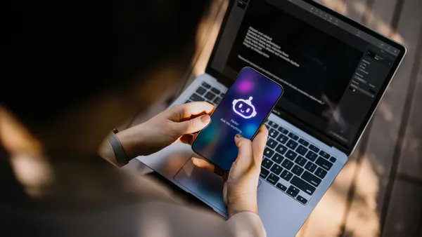 Businesswoman using Chatting AI chatbot virtual assistance app on smartphone to assist her while working on laptop in office park. Using AI technology at work. Online robot system. Concept of VR and AR technologies. People, AI, innovation and technology
