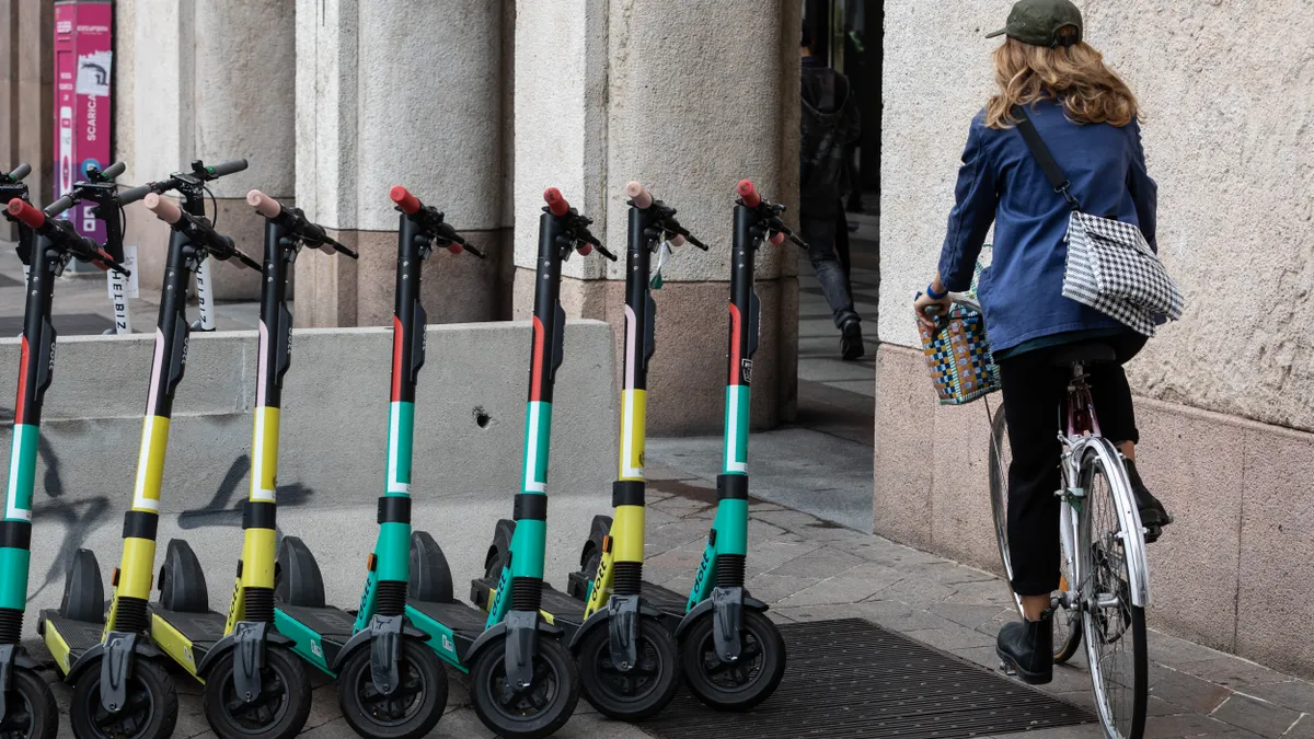 A woman rides her bicycle past a series of electric scooters of the Dutch scooter rental company DOTT on Piazza San Babila on September 23, 2020 in Milan, Italy.