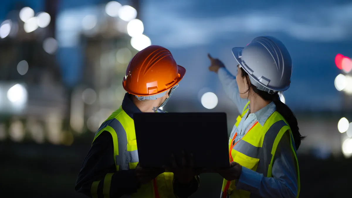 Engineers using laptops and working in front of a factory.