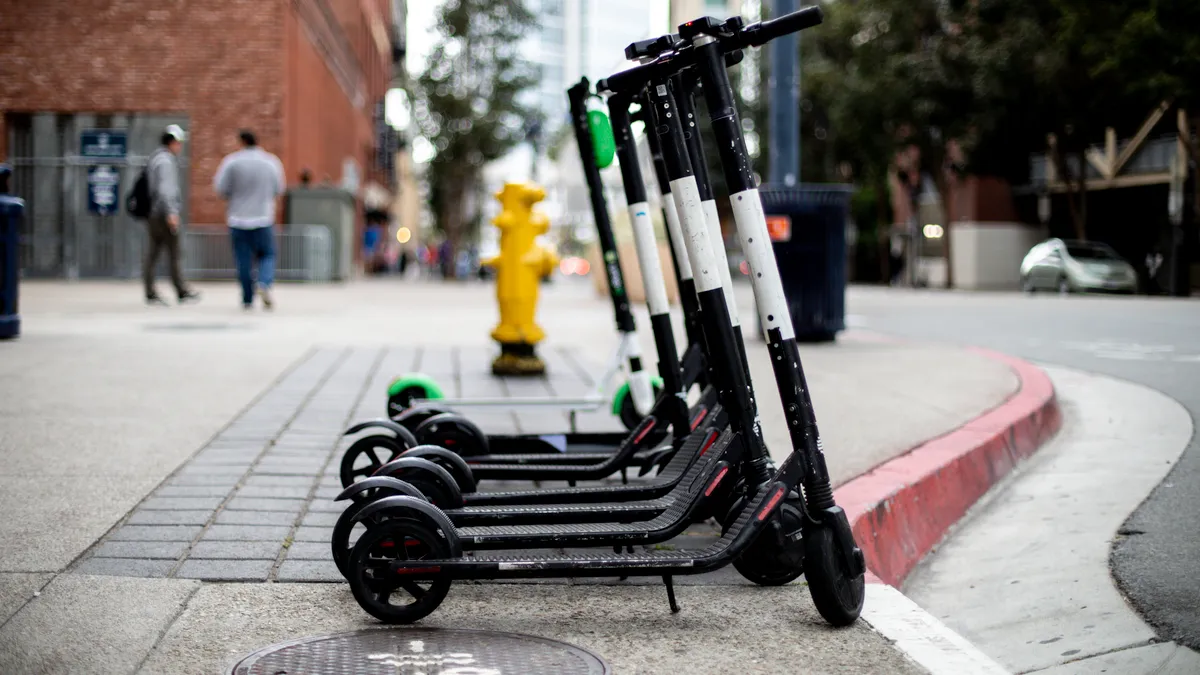 Electric scooters on a sidewalk in a city with people and buildings in the background.