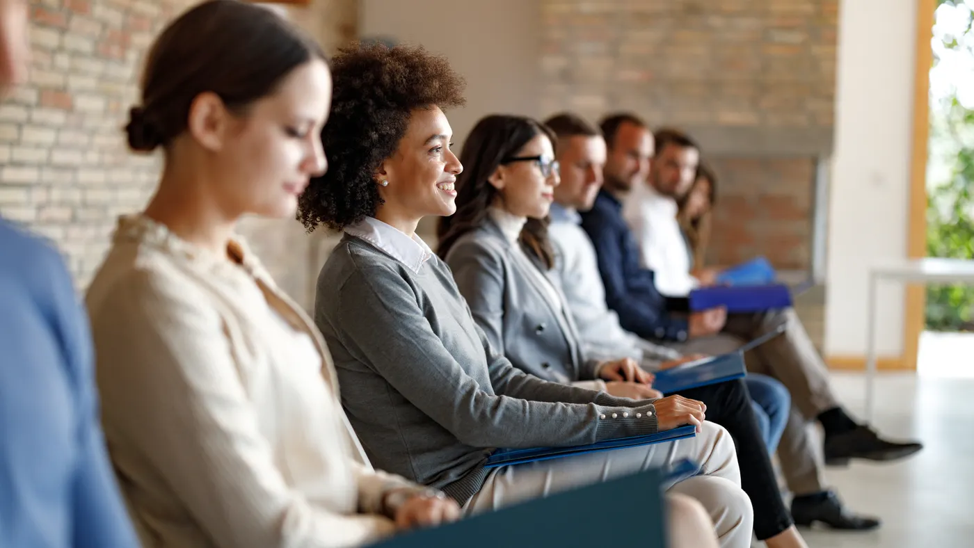 a row of job seekers seated in an office setting against brick wall