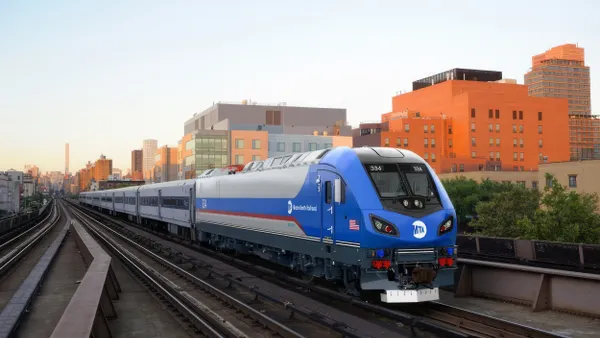 Illustration of a blue and white locomotive pulling a passenger train with city buildings in the background.