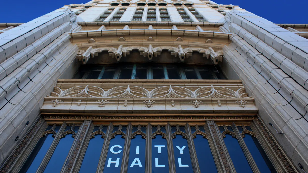 Shot looking up at the ornate facade of a building. Letters on the window read "City hall."