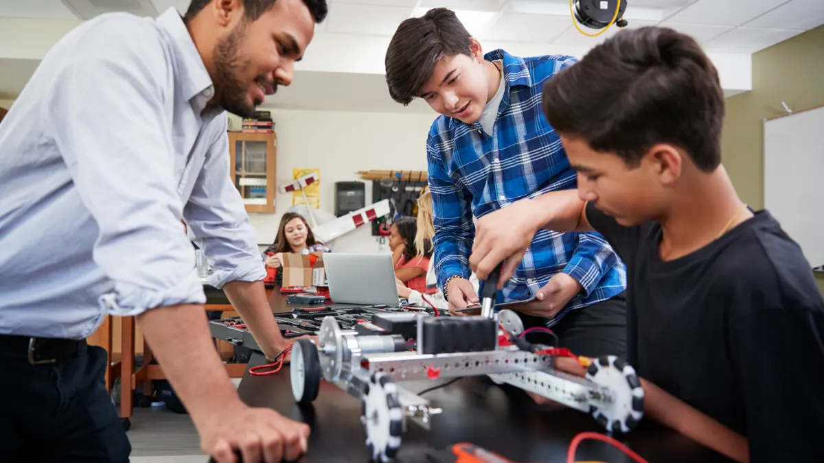 Two students and one adult gather around a lab table to observe a robot
