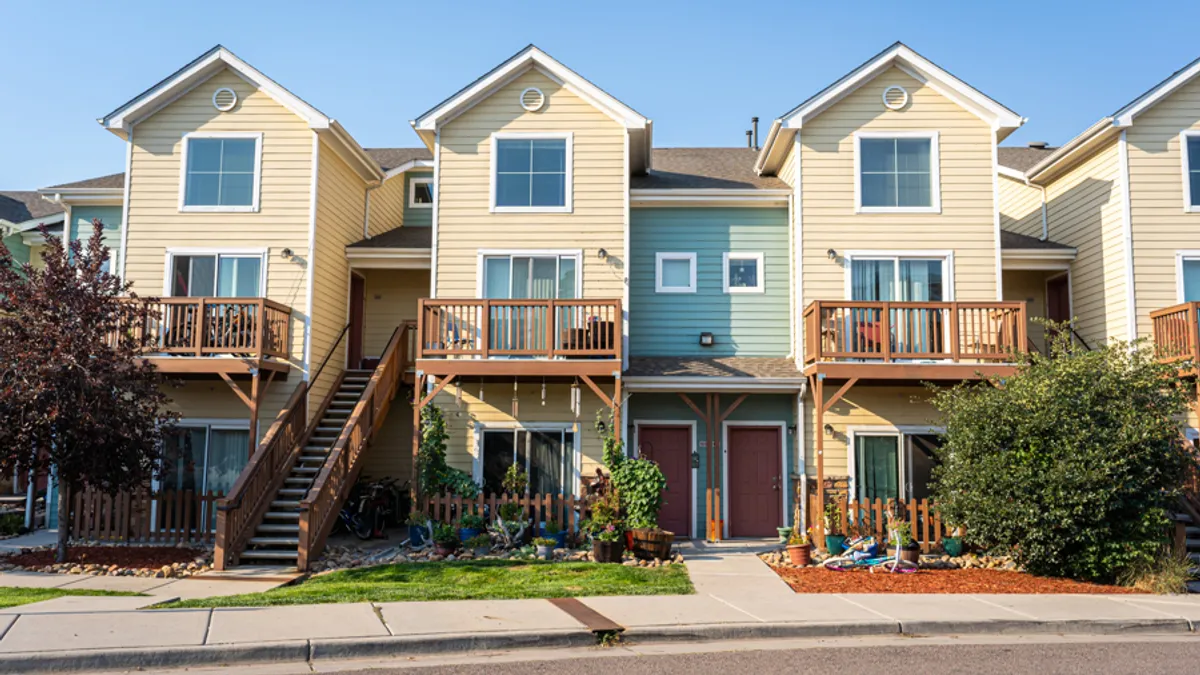 A three-story row of attached homes with yellow siding and red doors.