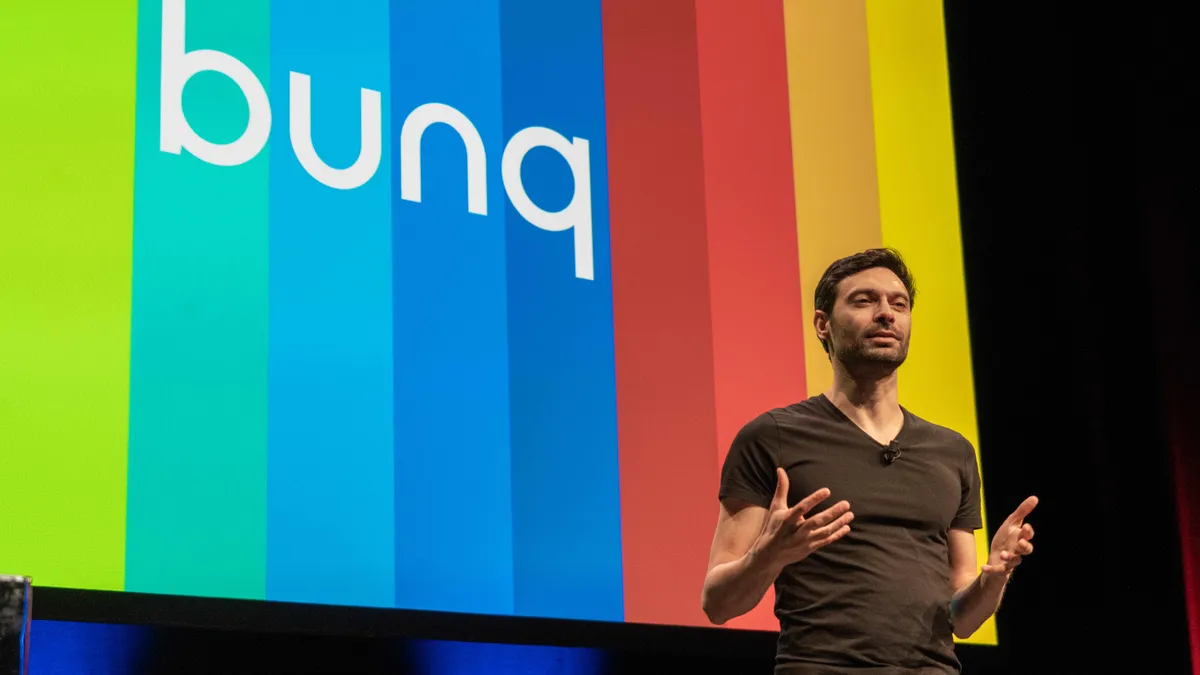 Bunq CEO Ali Niknam stands in front of Bunq's logo.