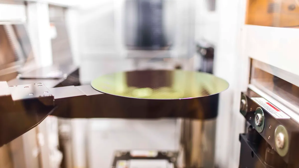 A gold, shiny reflective circular wafer being produced.