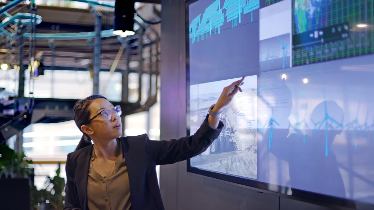 Woman conducting a presentation with data displayed on large screen.