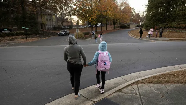 A parent crosses the street while holding her child's hand.