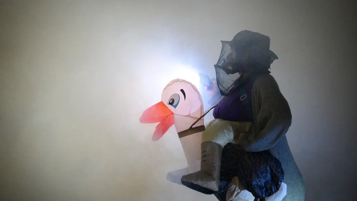 A person wearing a hat with a face covering and a inflatable duck costume surrounded by smoke.