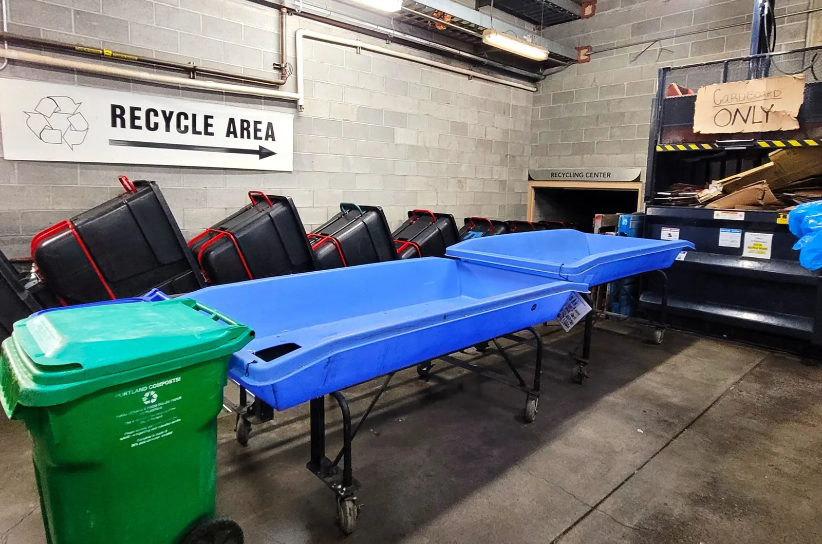 Blue sorting tables next to a green composting bin and other recycling infrastructure in a commercial business room.