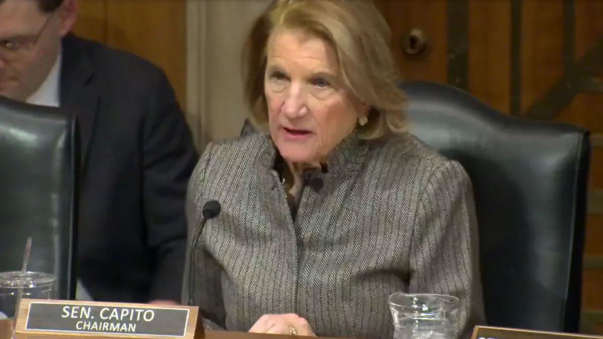 A woman speaks from a dias with a name plate saying Sen. Capito.