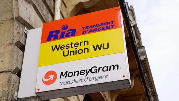 Exterior sign of a money transfer agency featuring logos for Ria, Western Union, and MoneyGram, mounted on a stone building in France.