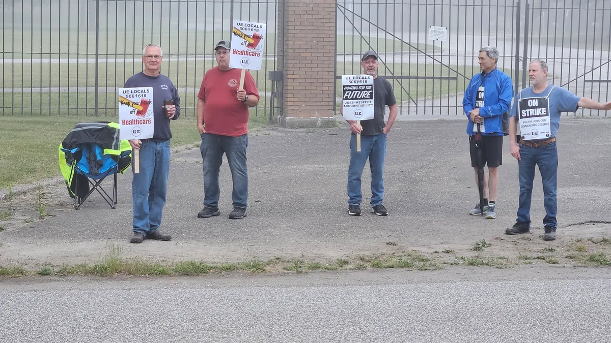 Five people standing in front of a gate picketing and holding UE strike signs on a foggy day.