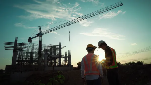 two engineers look at blueprints in front of a construction crane