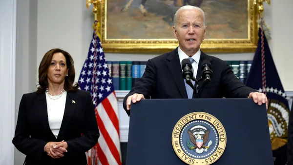 President Joe Biden delivers a speech at a podium while Vice President Kamala Harris stands in the background.