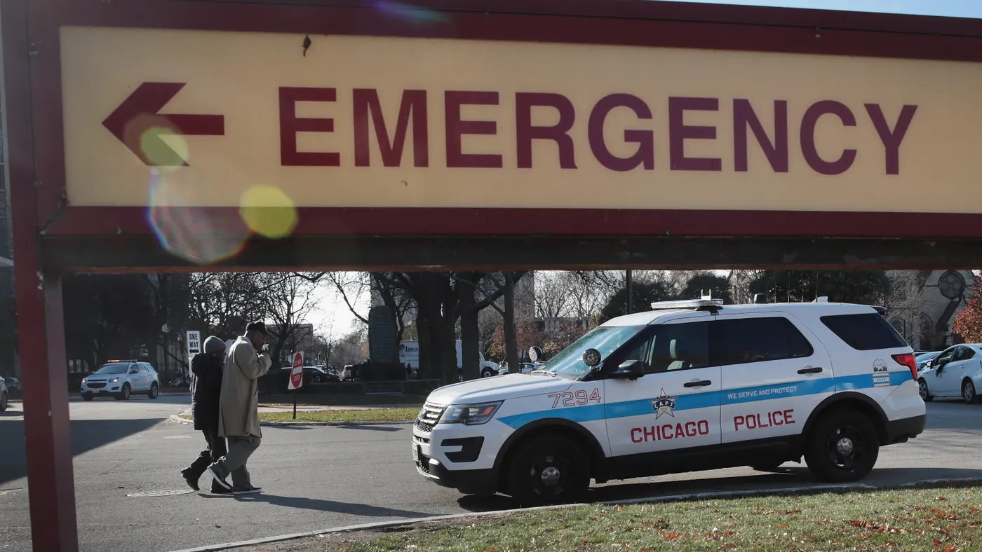 A chicago police department car sits in front of an emergency sign pointing to a hospital emergency room.