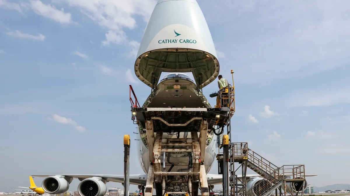 The nose of a Cathay Pacific cargo freighter is open with a cargo handler loading the aircraft.