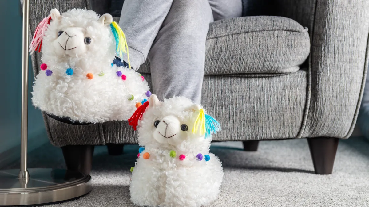 Young girl is wearing cute soft 3d llama slippers, while reading on the grey armchair