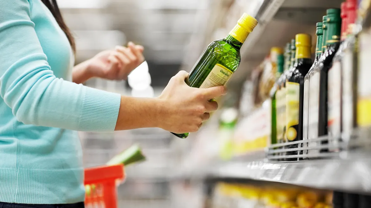 Person in grocery aisle choosing glass bottle