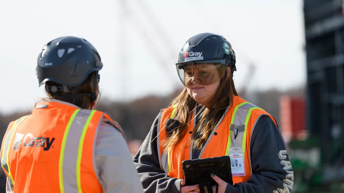 Two construction workers wear bright gear on a jobsite.