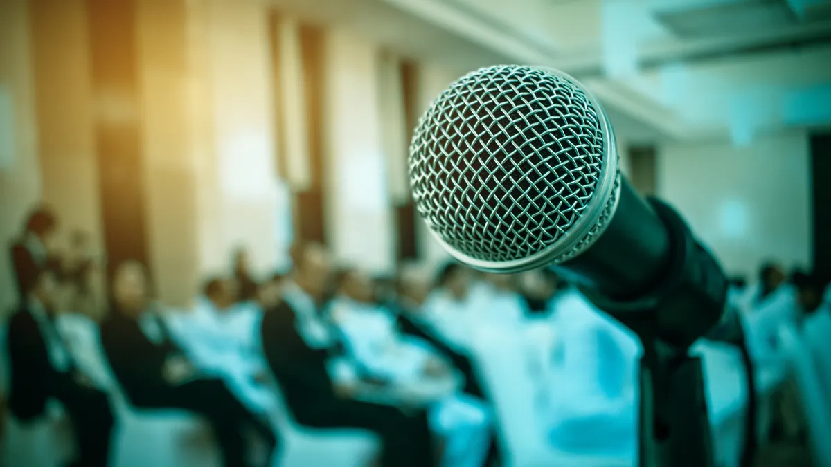 A microphone sits against a blurred background with people sitting down.