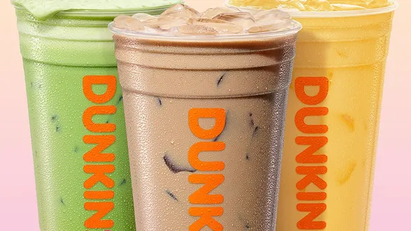 Three Dunkin' drinks with a brown drink in the foreground and a green drink and orange drink in the background.