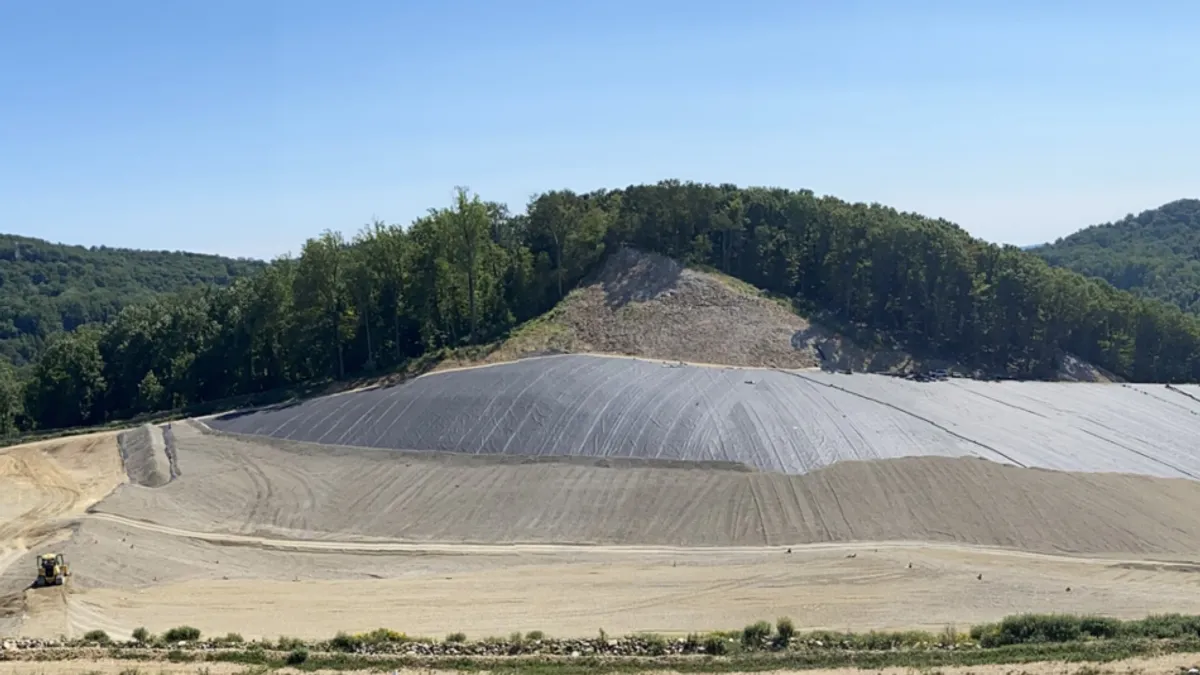 A large mound devoid of vegetation with a small dumpster in the corner