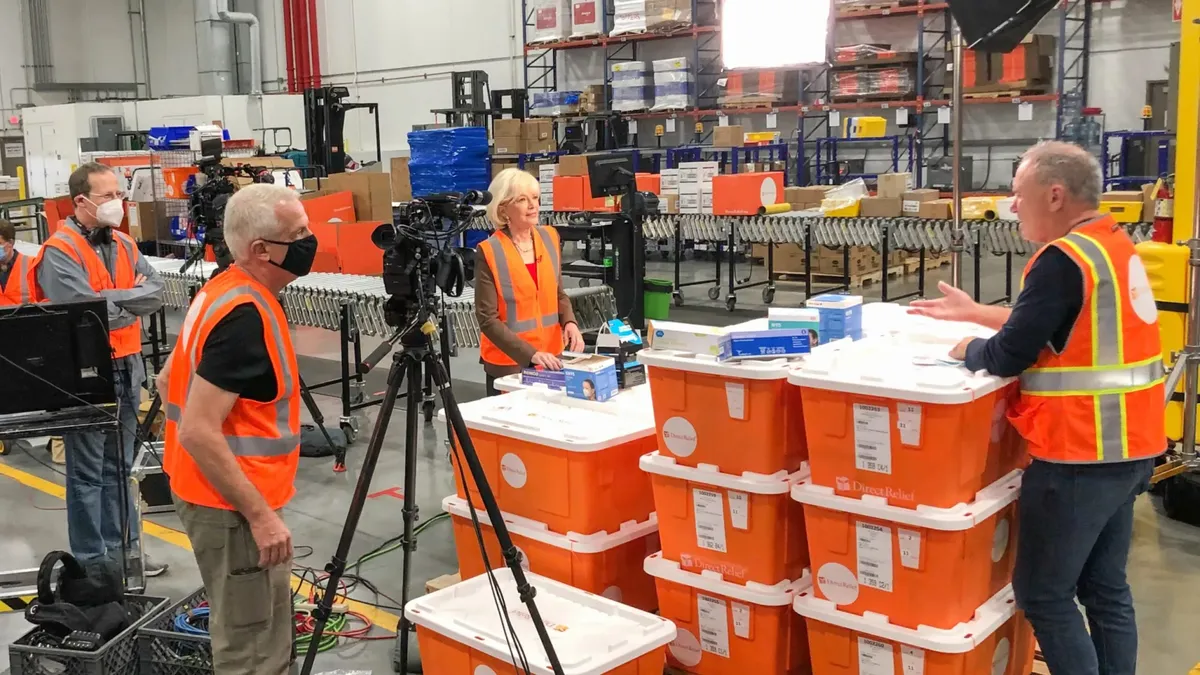 Warehouse workers for Direct Relief stand around containers of supplies.